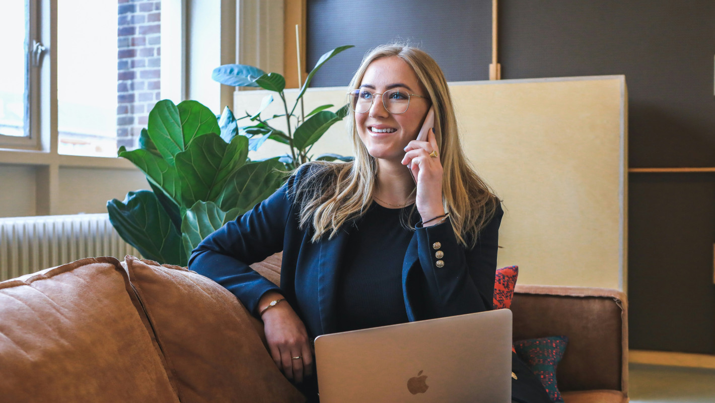 Frau wartend mit Handy und Laptop auf einer Couch