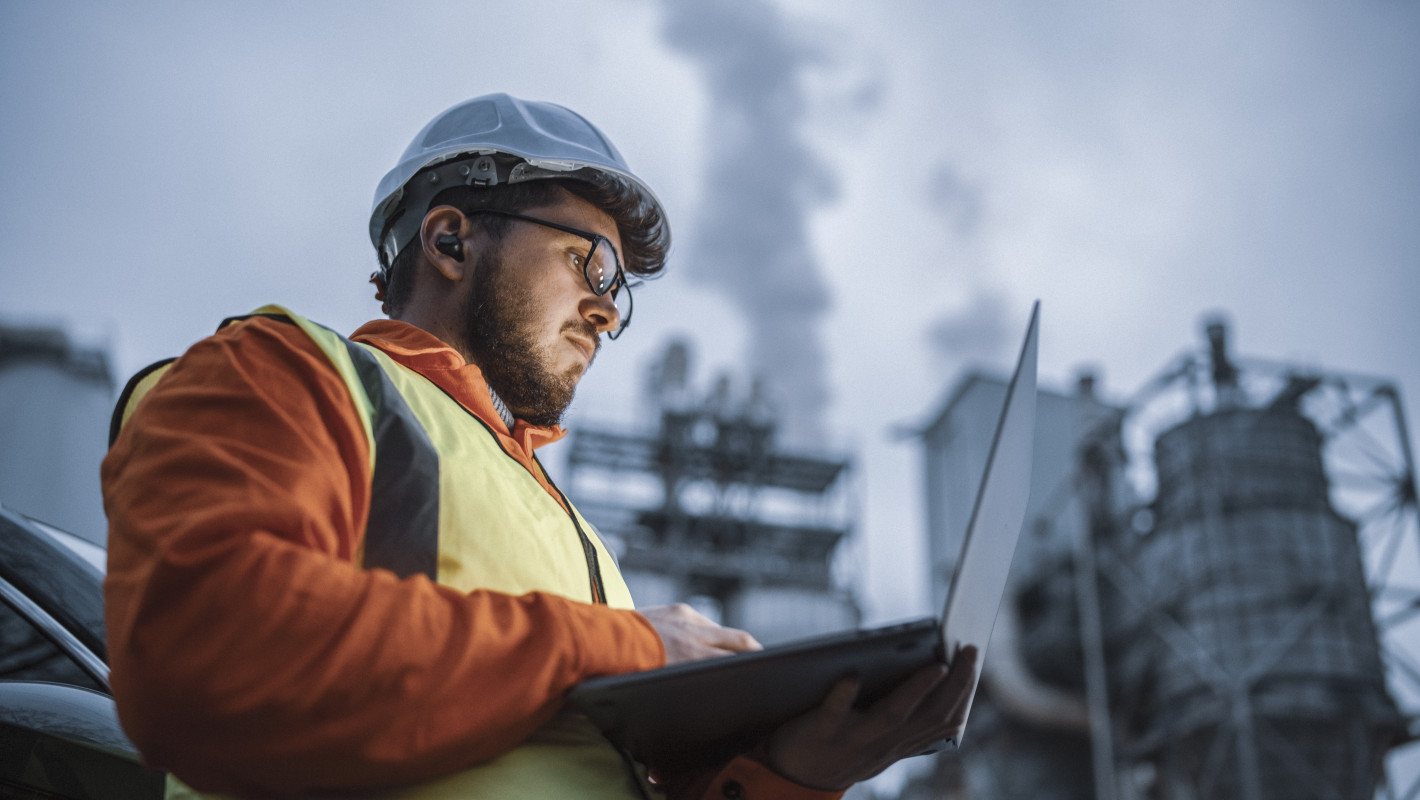 Arbeiter prüft etwas am Laptop vor einer Fabrik