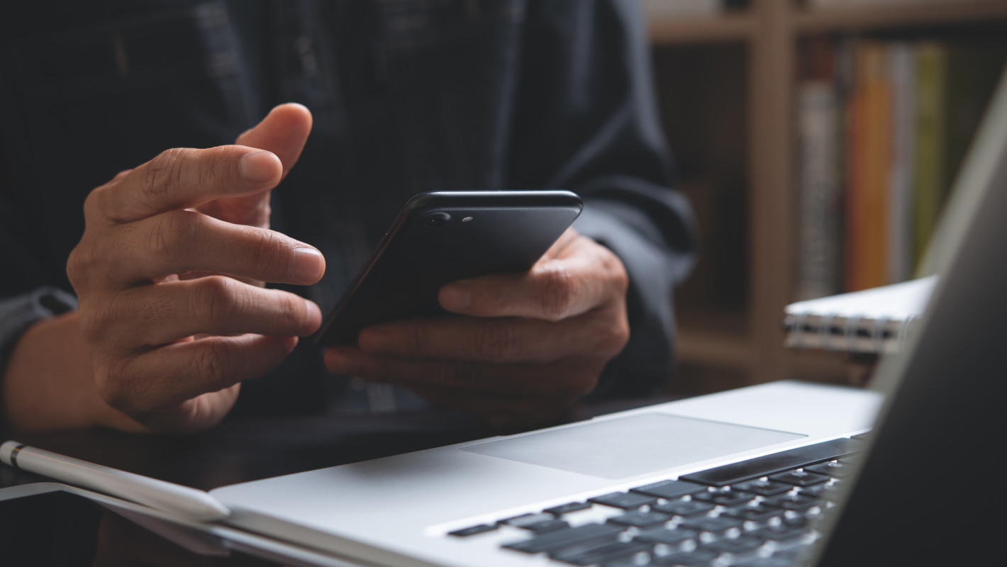  Man checking cell phone in front of laptop