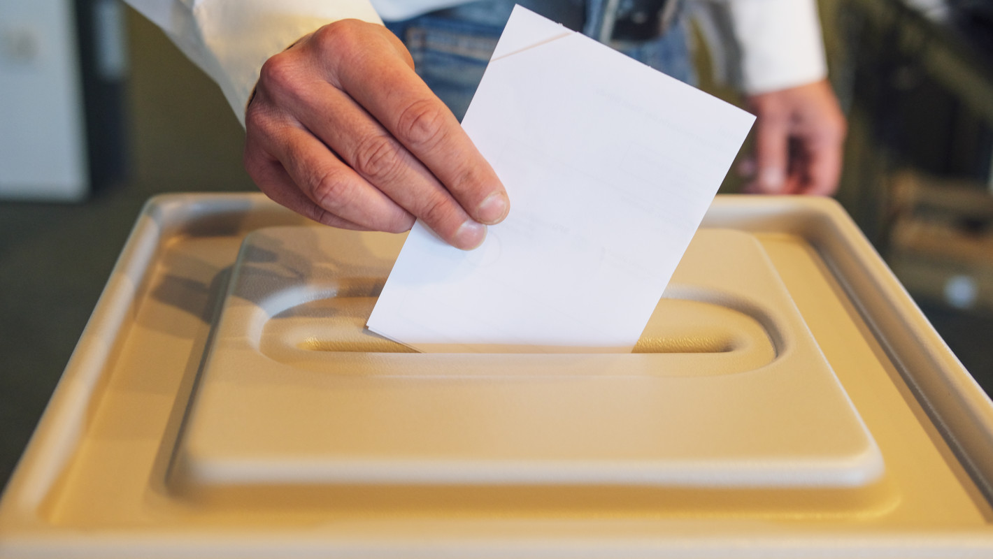 Mann steckt seinen Wahlschein in die Box