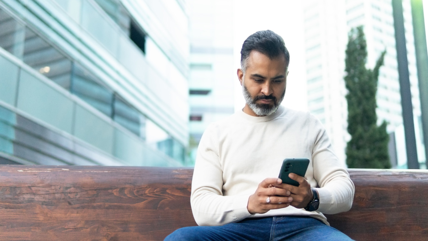 Man uses his smartphone on a bench