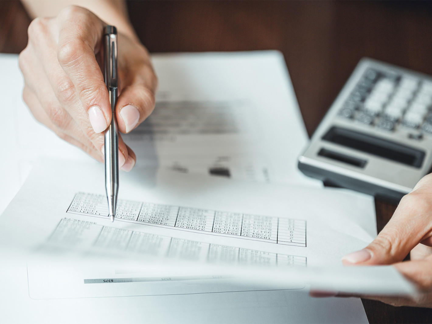 Person prüft eine Zahlentabelle auf einem Zettel, daneben ein Taschenrechner