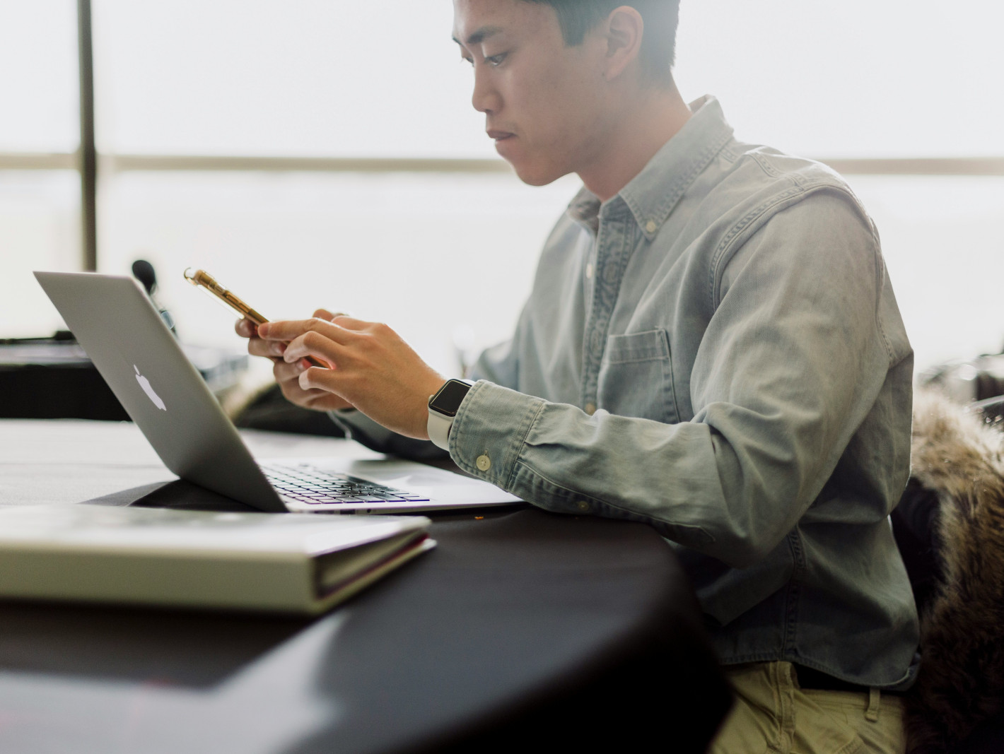 Mann sitzt grübelnd über Handy mit Laptop am Tisch
