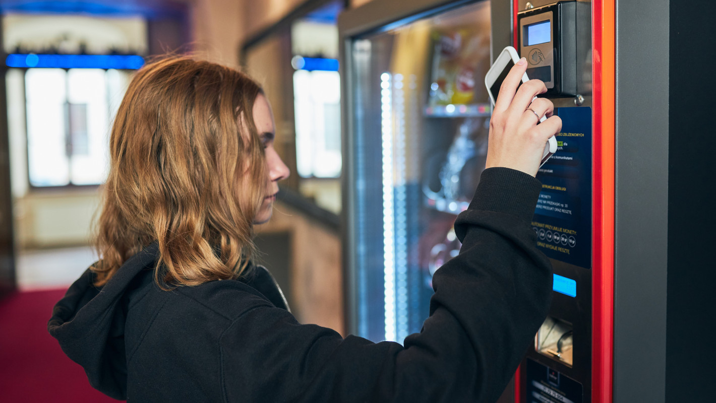 Mädchen bezahlt mit ihrem Smartphone an einem Automaten
